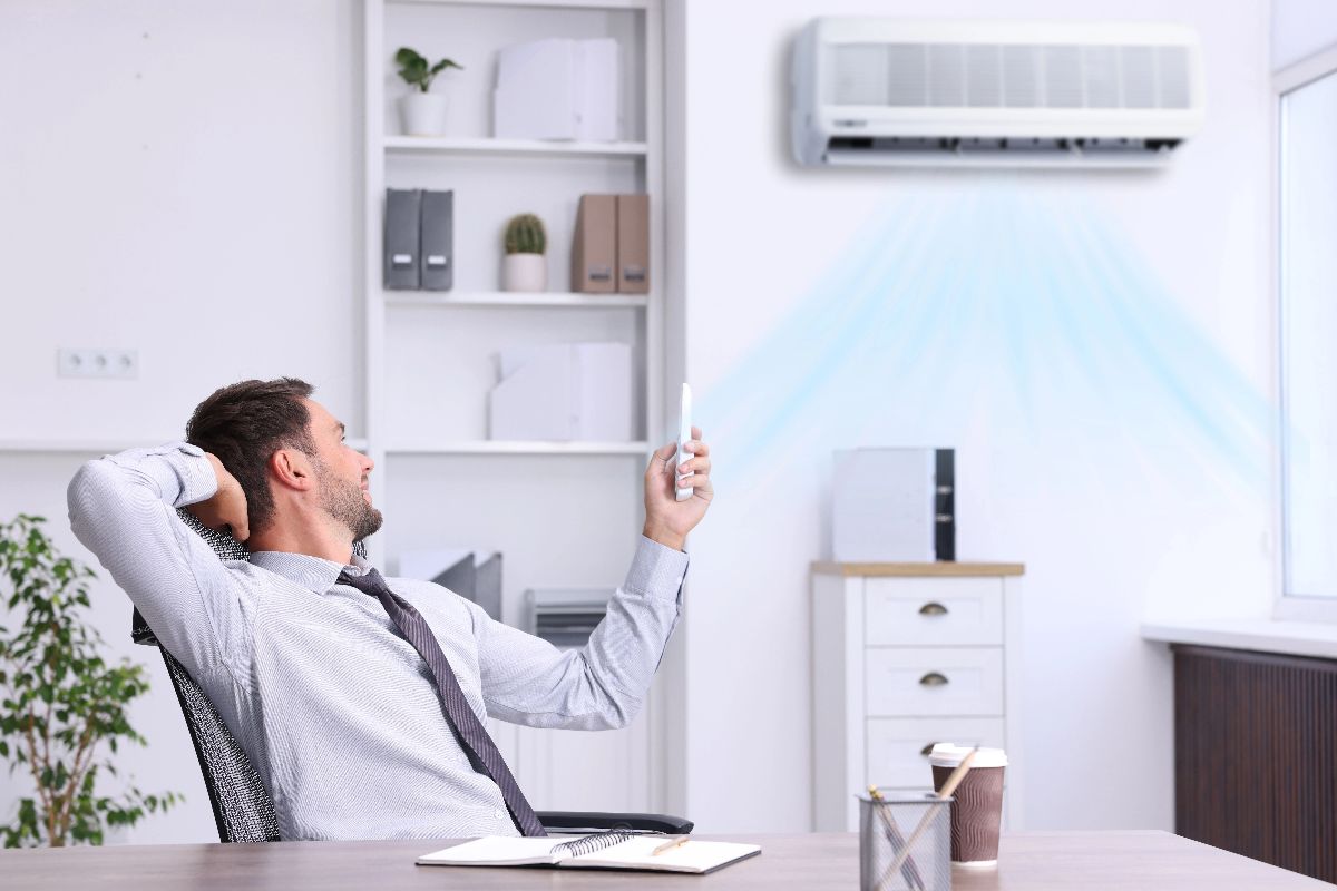 Man using a remote control for a wall-mounted air conditioner in an office