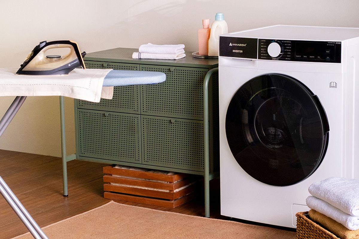 Hanabishi inverter front-load washing machine beside an ironing board and folded laundry in a compact home laundry area